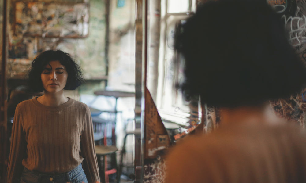 A woman looking at herself in the mirror, symbolizing self-reflection and the journey of overcoming self-doubt.